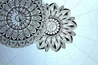 this is the image of a mandala and another one being sketched on a mandala grid behind the first mandala