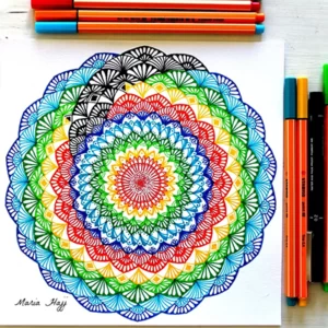 Colorful mandala drawn on a white paper, with colored pens beside it on the table