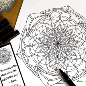 A mandala drawn with black ink on white paper, with ink pens on the table besides it.